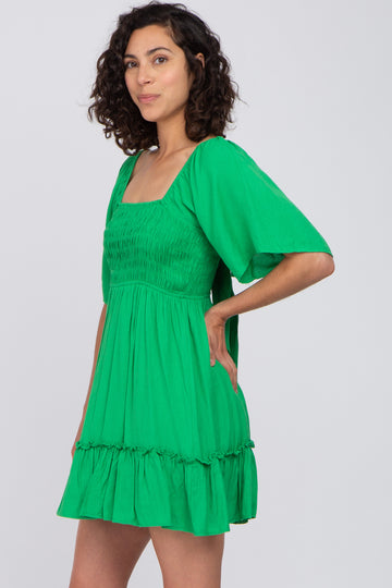 woman with curly hair wearing a green smocked mini dress with flutter sleeves and a square neckline