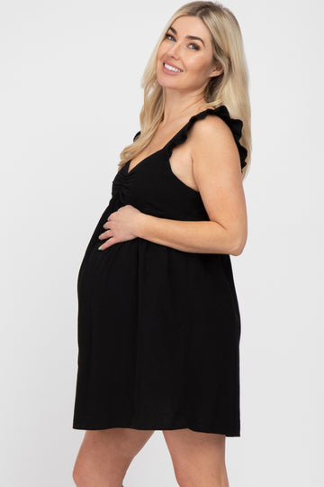 smiling pregnant woman in a black sleeveless maternity dress with ruffle straps against a white background