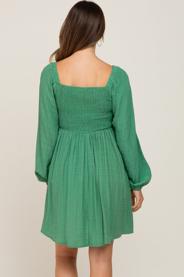 Back view of a woman wearing a green long sleeve mini dress with a smocked bodice and square neckline