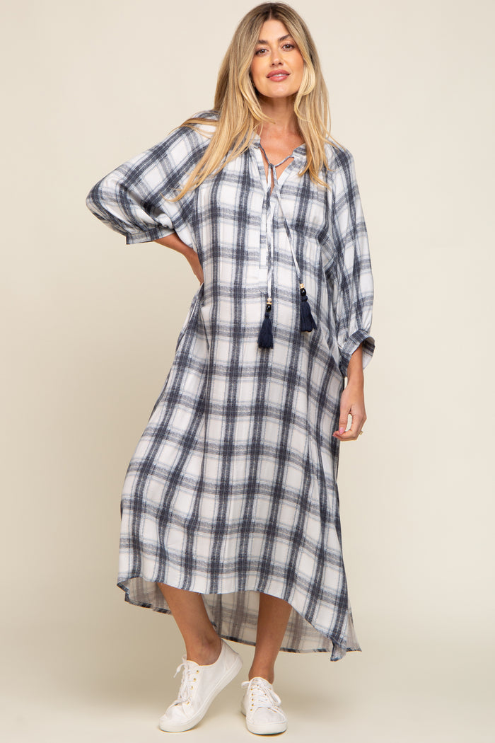 Woman wearing a white and navy plaid maternity midi dress with tassel ties and white sneakers