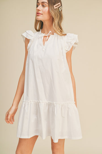 woman wearing a white short sleeve mini dress with ruffle details and a tie neck