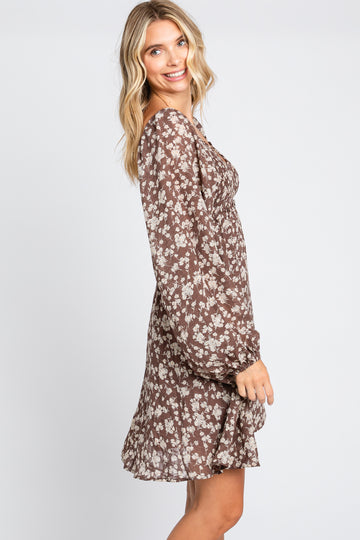 Woman wearing a brown long sleeve floral mini dress with smocked bodice and ruffled hem