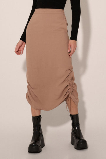 woman wearing a beige ruched midi skirt with side drawstrings and styled with black chunky-heeled boots